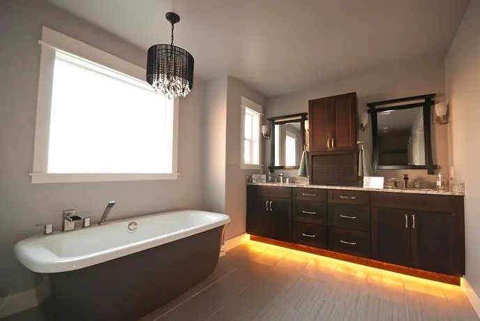 A bathroom with a tub , sink , mirror and window.