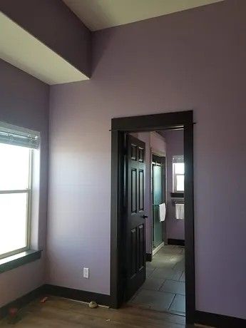 A room with purple walls and a black door leading to a bathroom.