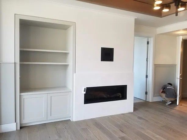 A man is kneeling in a living room with a fireplace and shelves.
