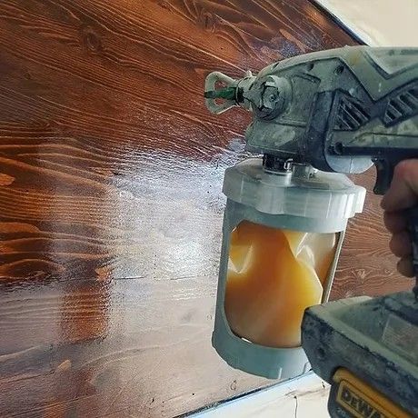 A person is using a paint sprayer to paint a wooden surface.