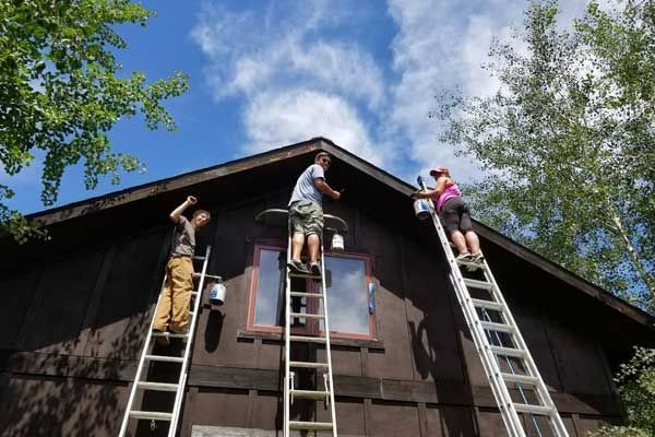 A group of people are painting a house with ladders.