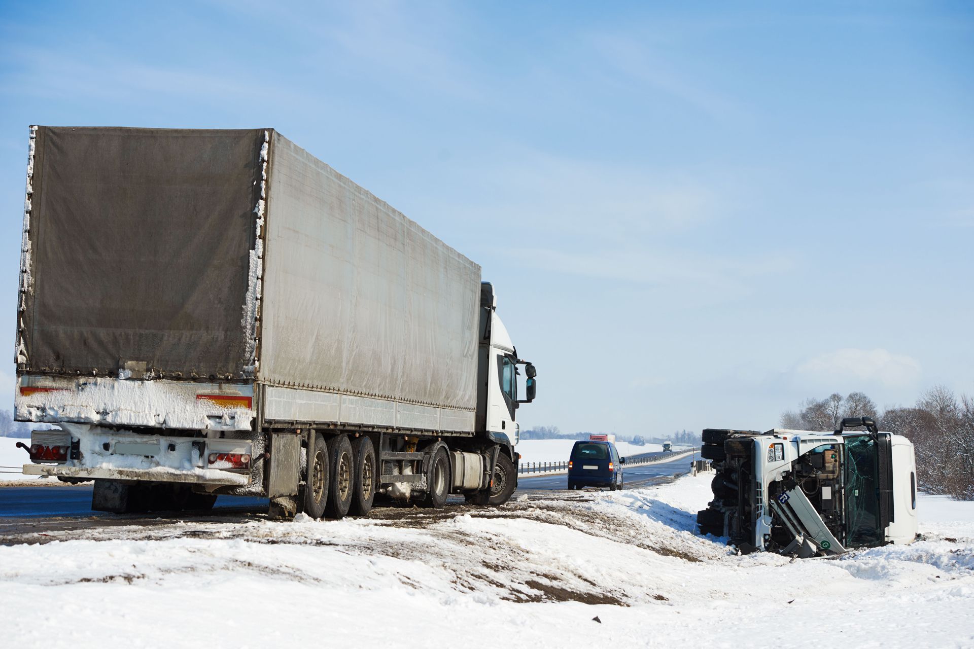 Overturned truck on snowy roadside with another semi nearby in winter conditions