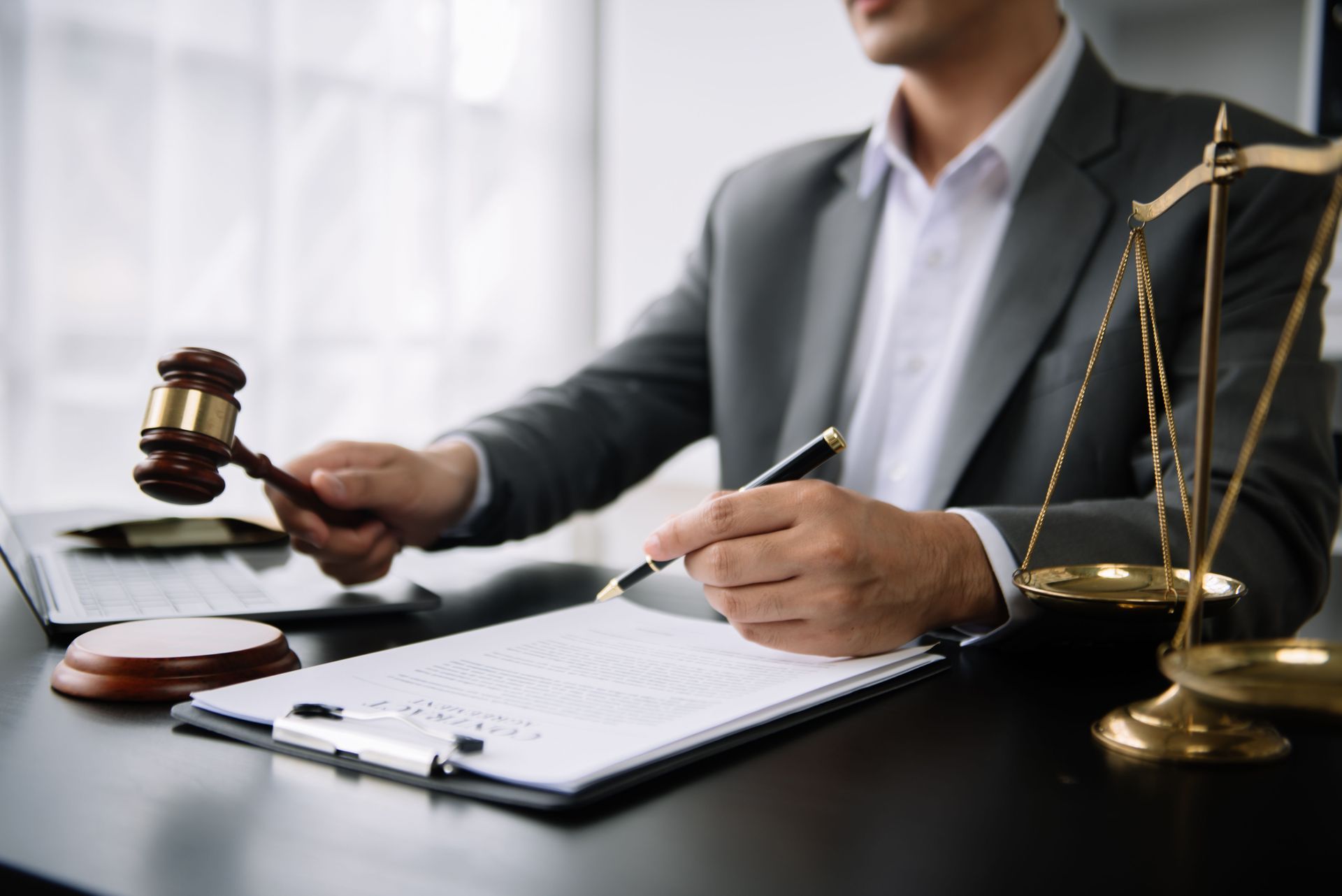 Lawyer at desk holding gavel beside scales of justice and an open notebook