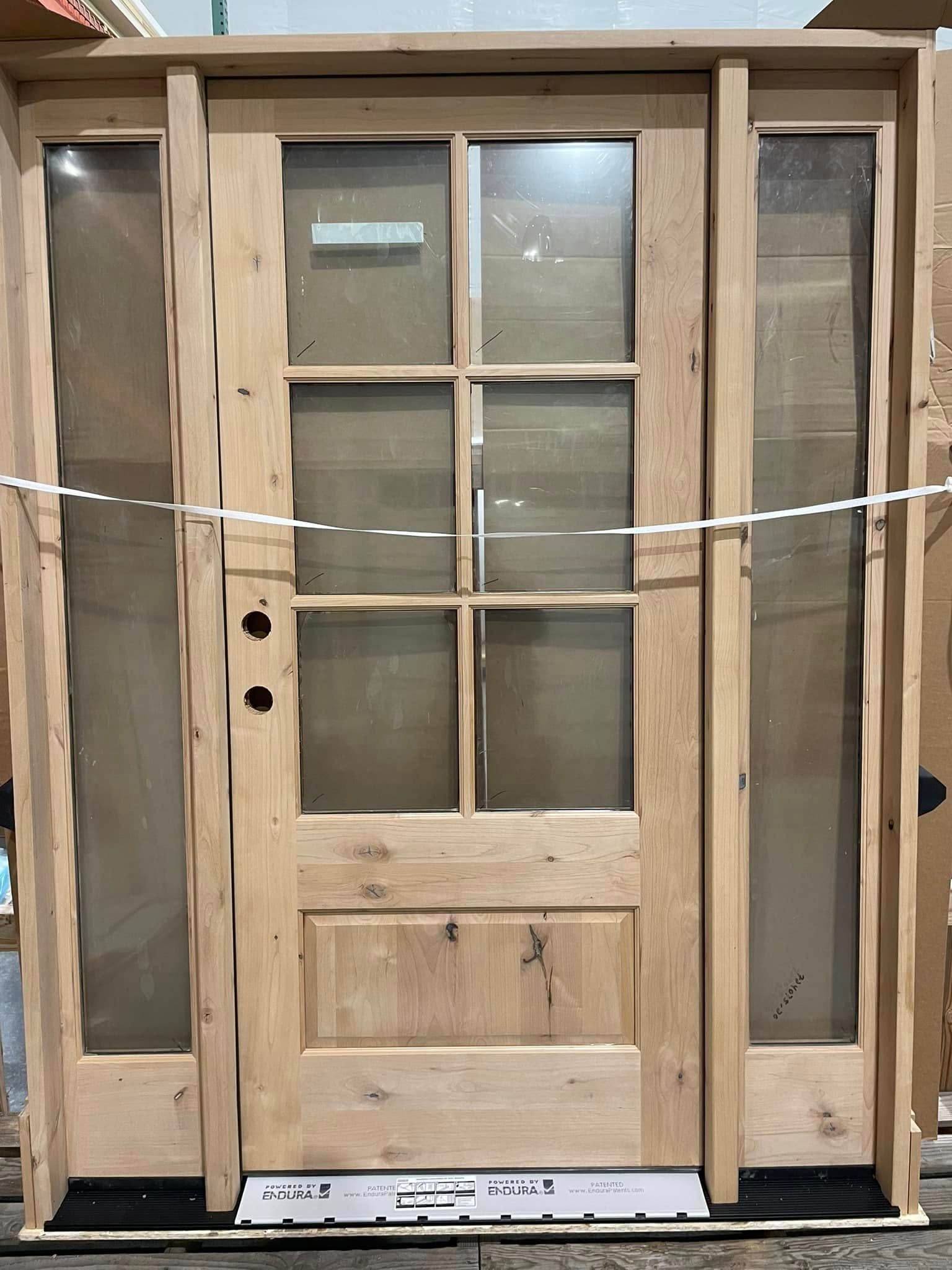 Wooden front door with glass panes and side panels, light brown, in a warehouse setting.