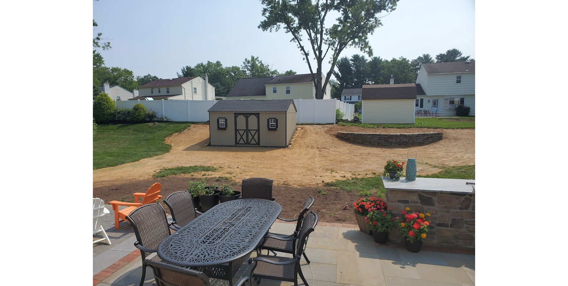 Backyard patio with table and chairs overlooking a landscaped yard and small playhouse/garage