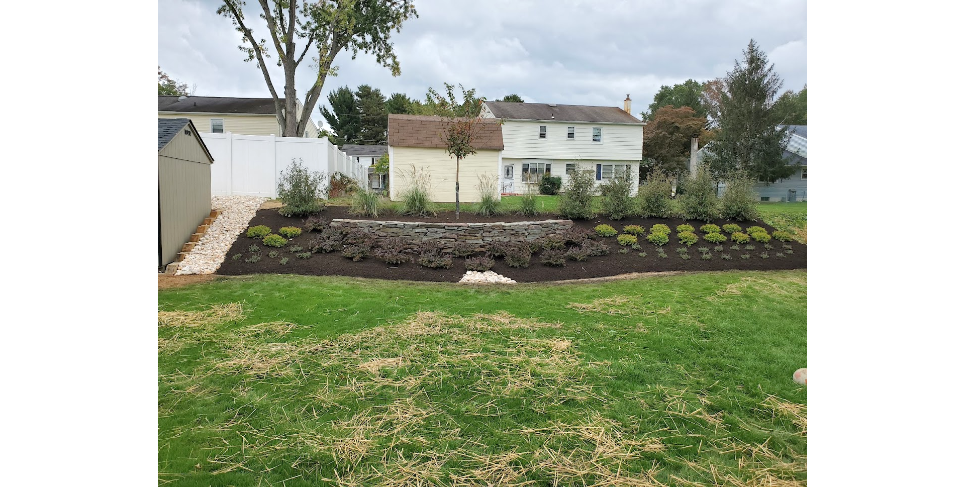 Stone retaining wall and white houses behind a green lawn under cloudy sky