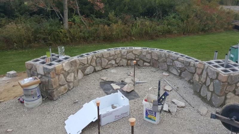 Stone outdoor fire pit under construction with curved retaining wall and scattered tools on a patio