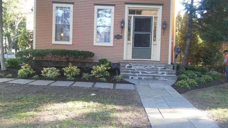 Front of a brick house with a stone walkway, steps, and shrubs along the facade.