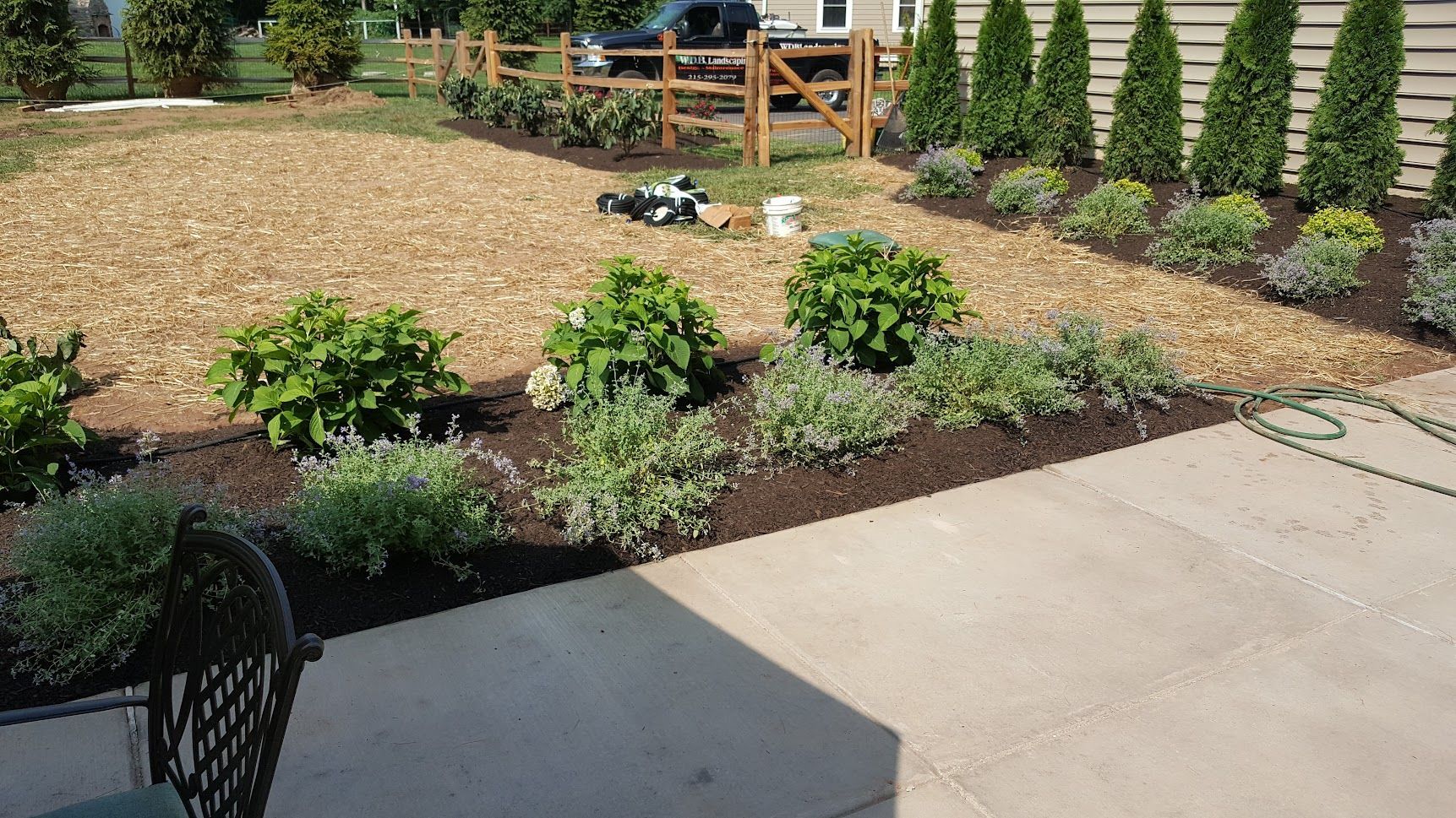 Landscaped garden bed with shrubs and mulch beside a concrete patio and wooden deck