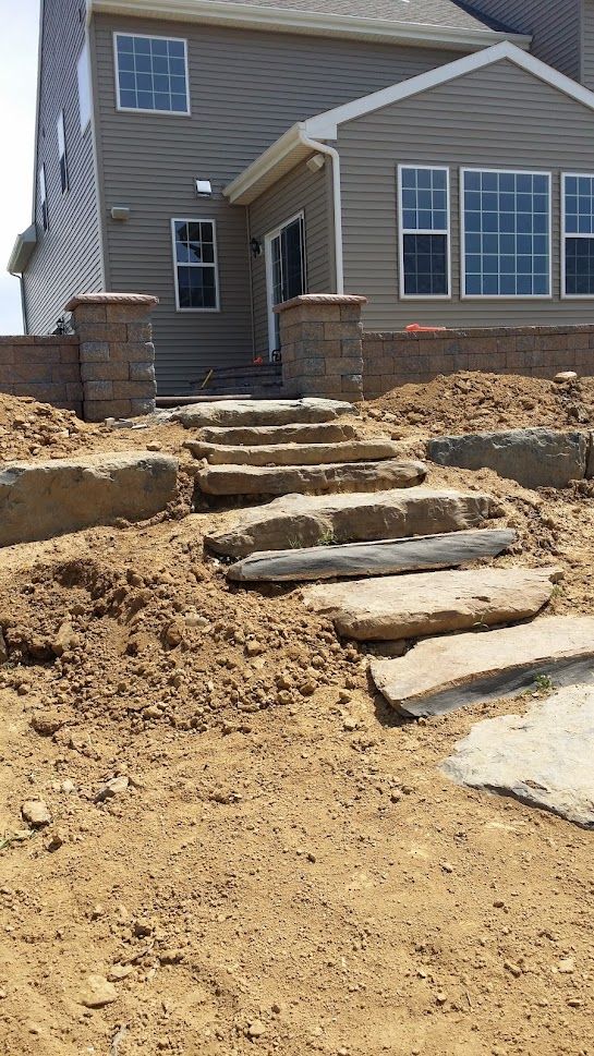 Stone step path leading to a house entrance across a dirt yard under construction