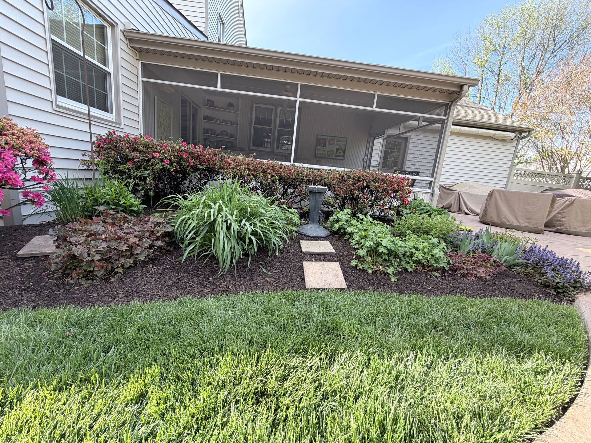 Front yard garden with shrubs, stone path, and a covered porch beside a house