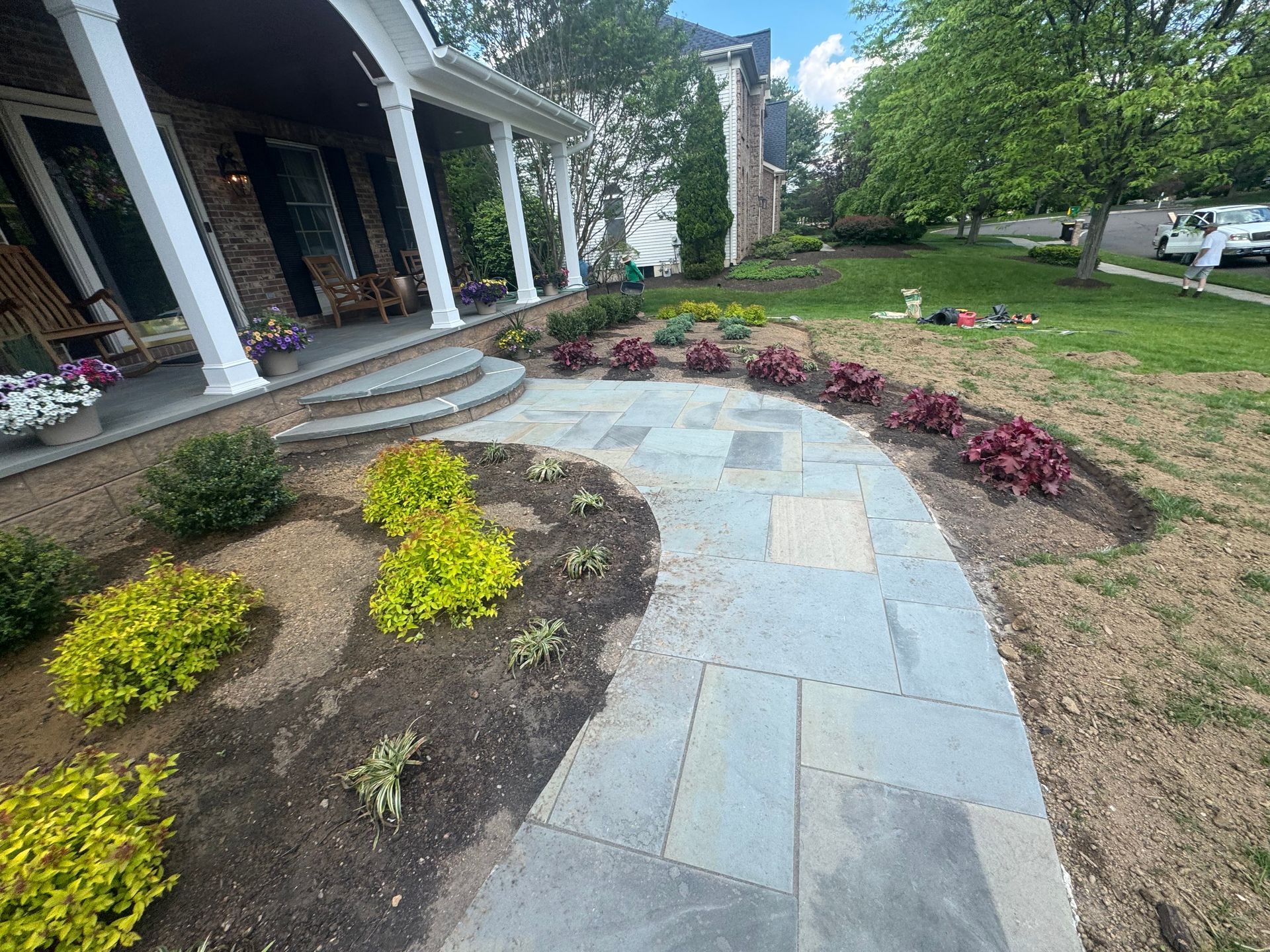 Curved stone walkway through landscaped front yard with yellow and red shrubs beside a porch