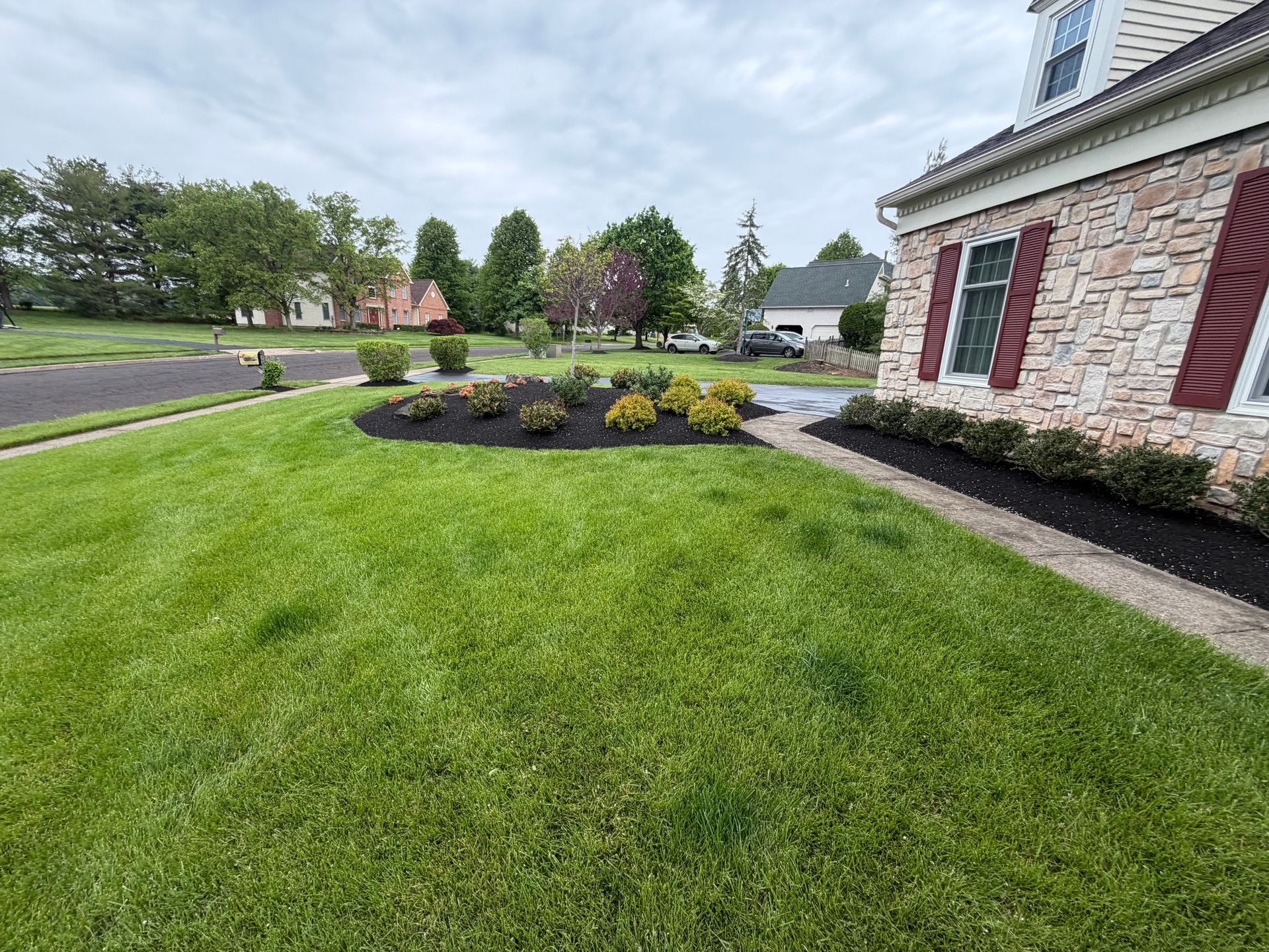 Suburban home with manicured lawn, flower beds, and stone siding on an overcast day