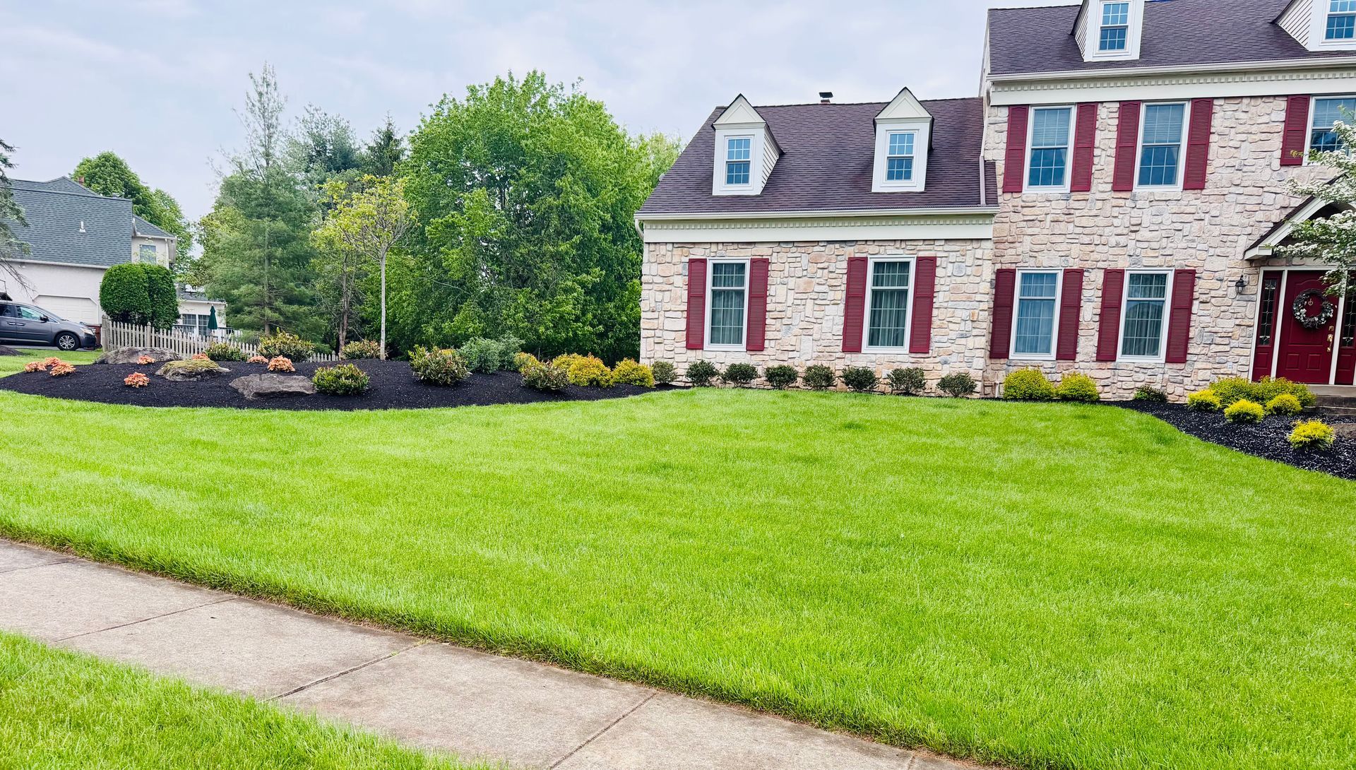 Suburban house with red shutters, manicured lawn, and a sidewalk in front