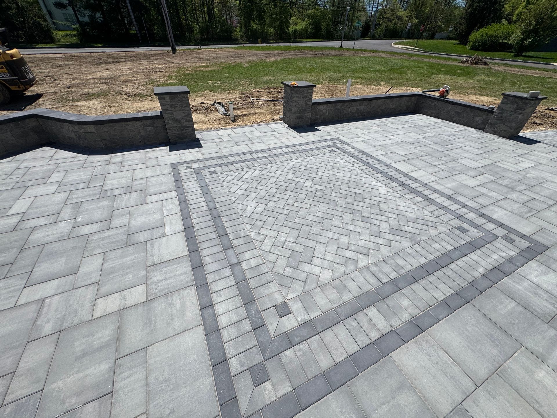 Stone retaining wall bordering a garden bed with green plants, asphalt path in foreground.