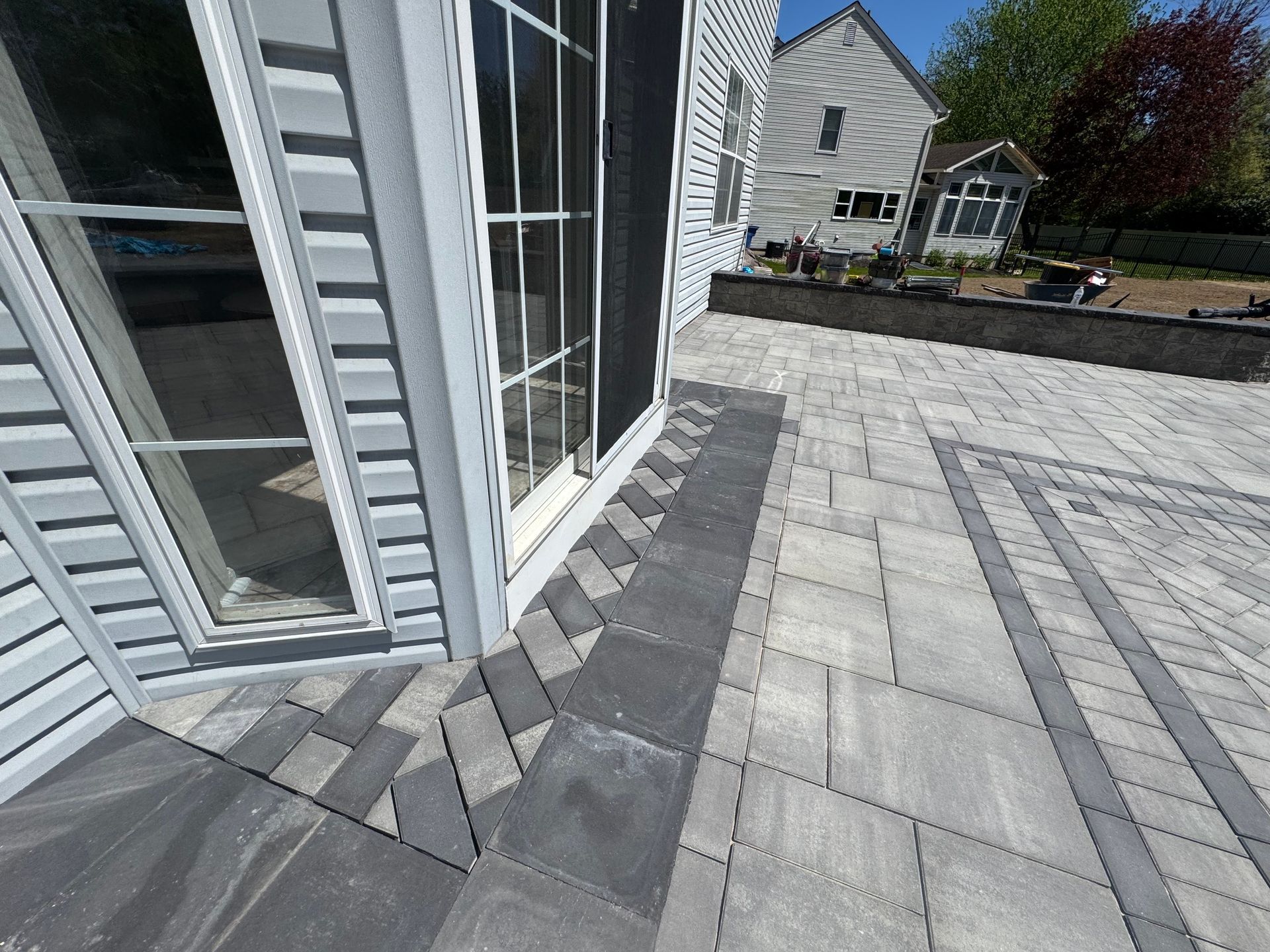 Stone patio beside a white house with gray pavers and a raised deck area