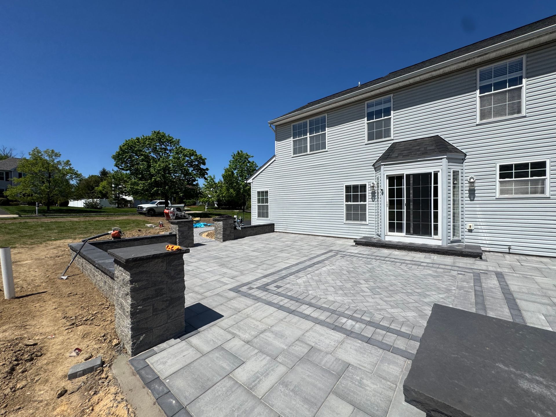 Backyard patio with gray pavers, stone retaining walls, and white French doors on a house