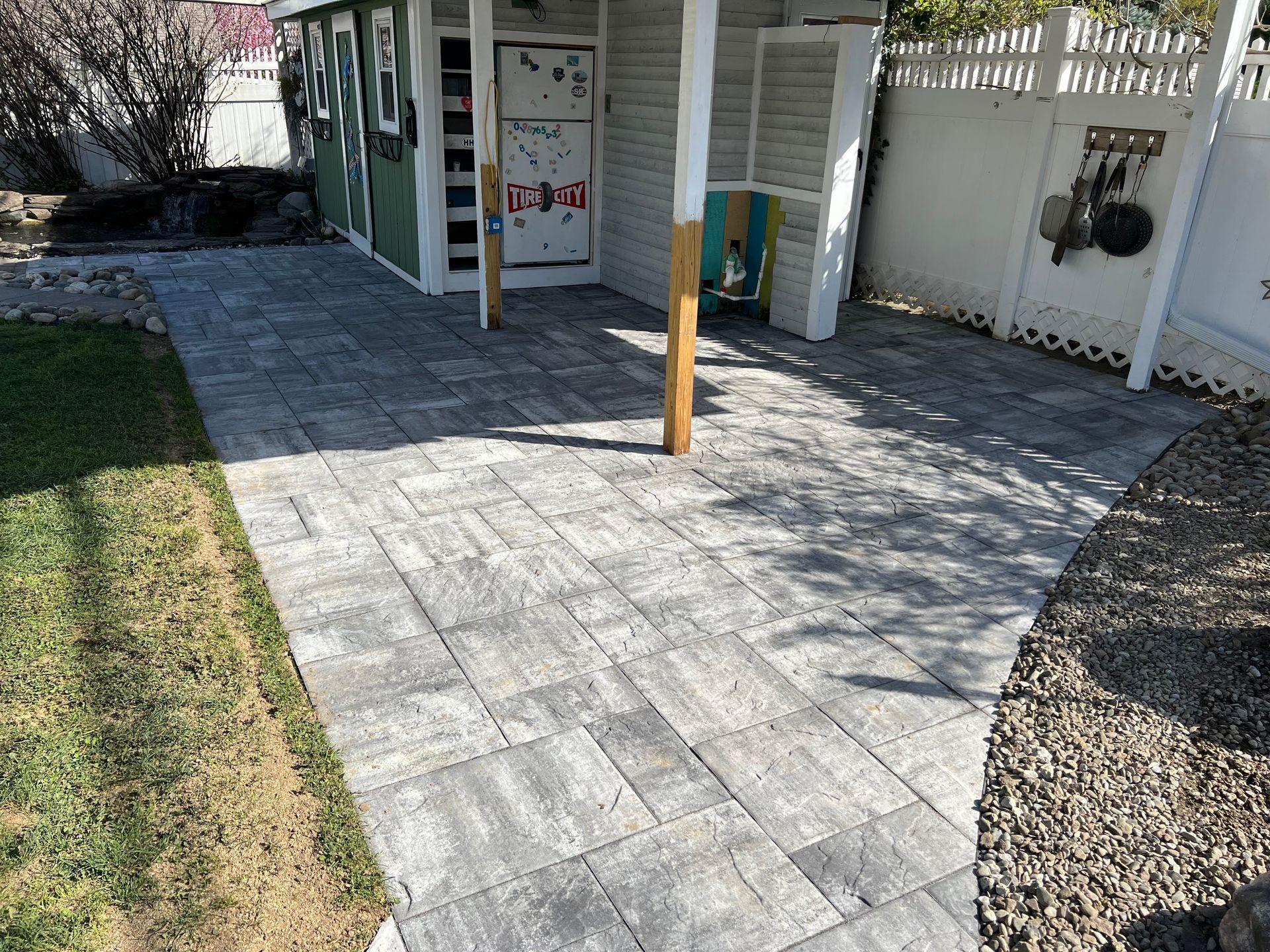 Freshly paved stone patio outside a building with a wooden post and small garden edges