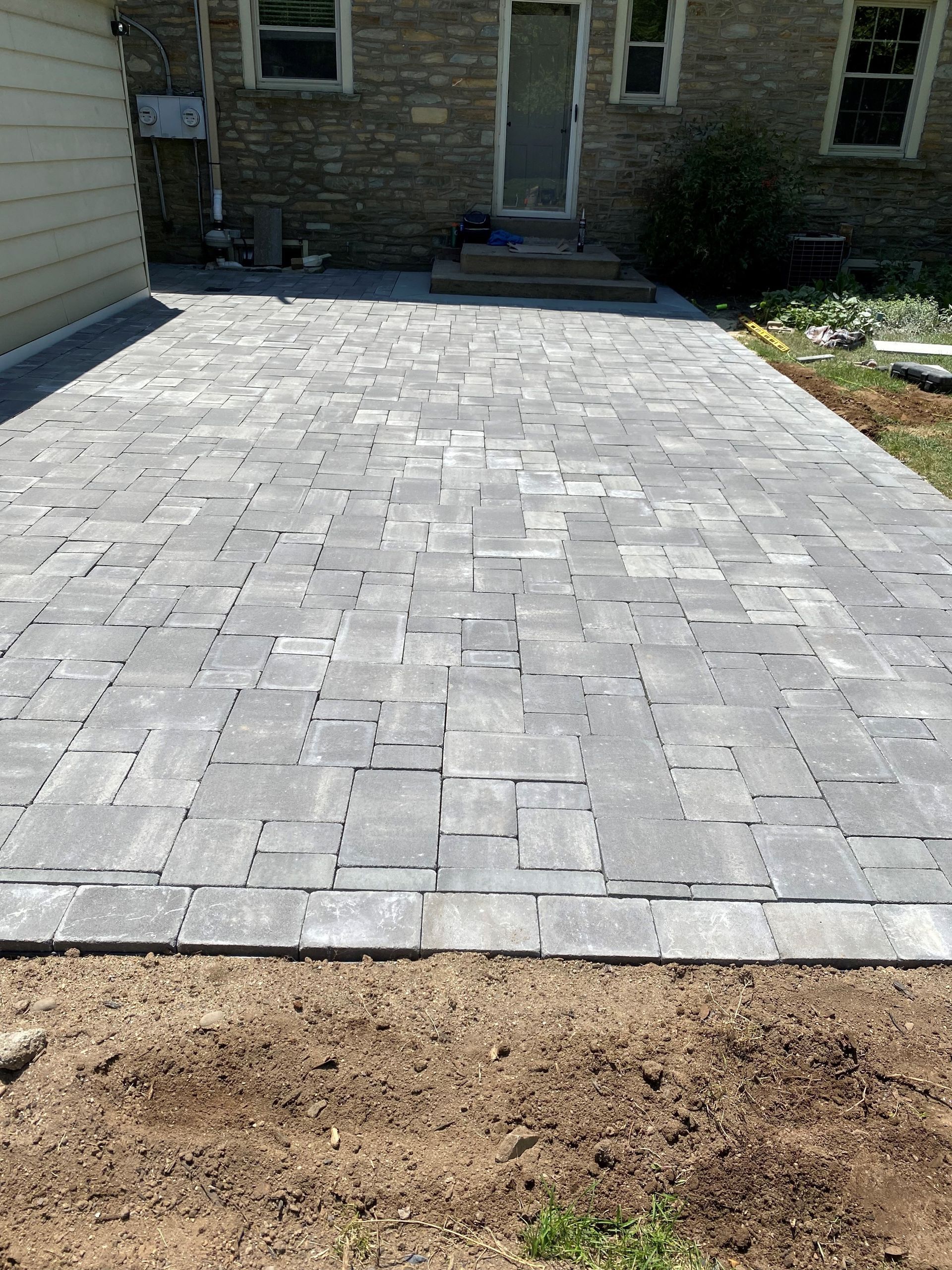 New gray paver patio leading to a brick house entrance