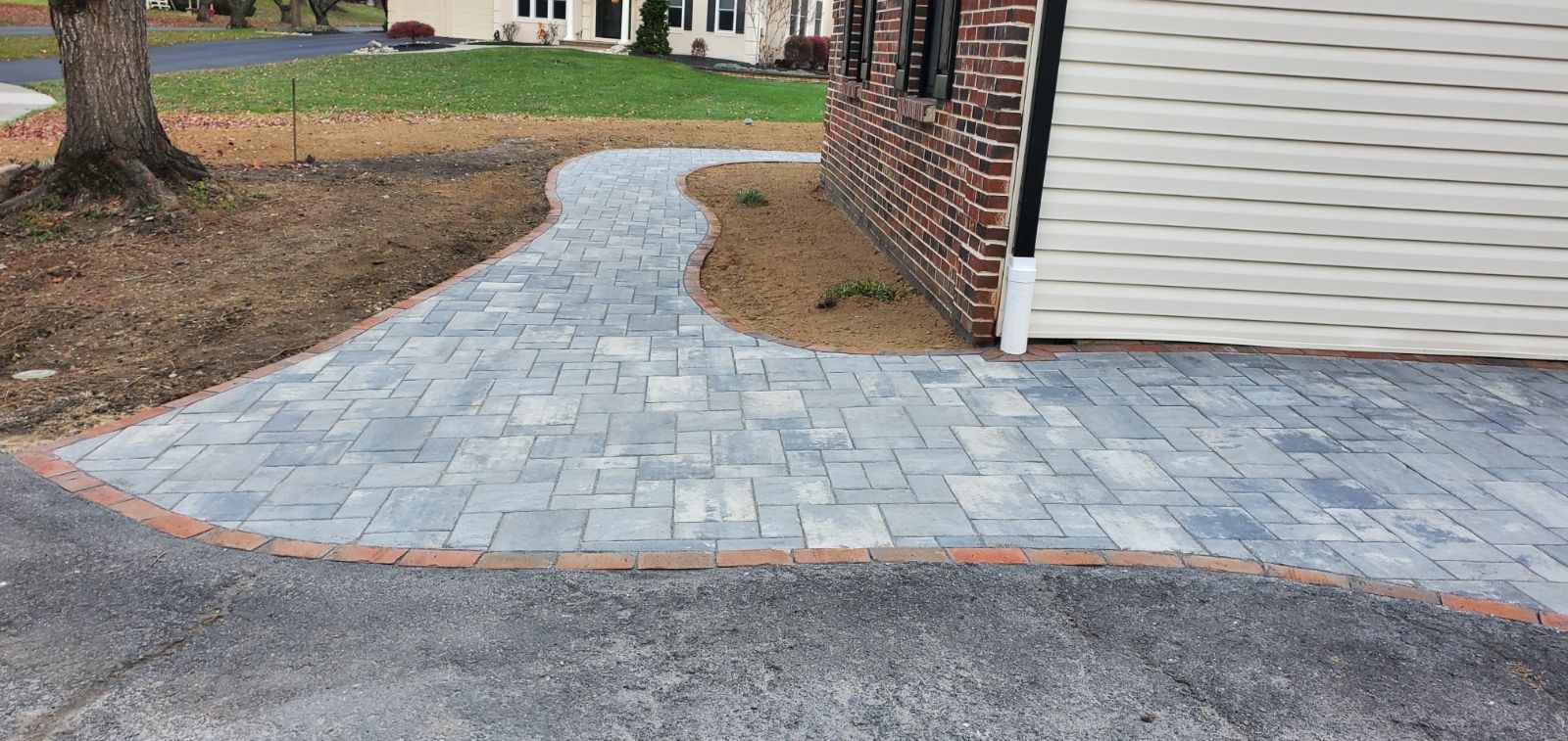 Paver walkway curving to a house beside a driveway and lawn in a suburban yard