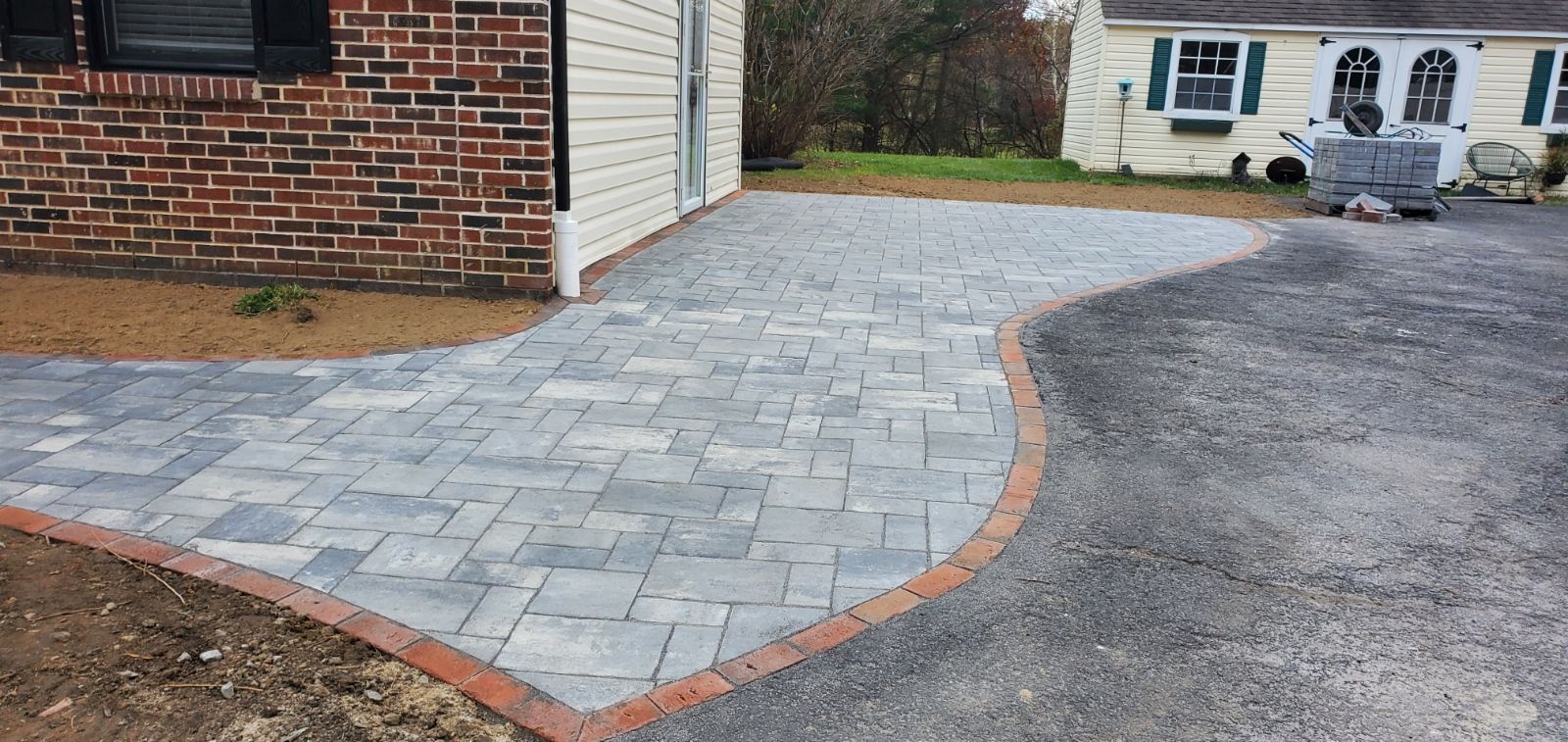 Stone paver driveway beside a brick house, bordered by a gravel drive and curb edging