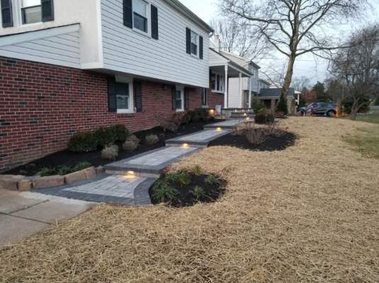 Apartment walkway with small garden beds beside a brick building and dry winter grass