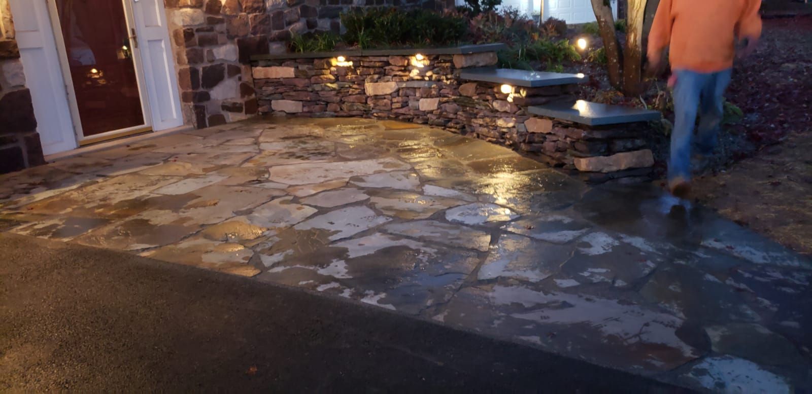Stone patio and steps outside at dusk, with a person in an orange shirt standing near the walkway.