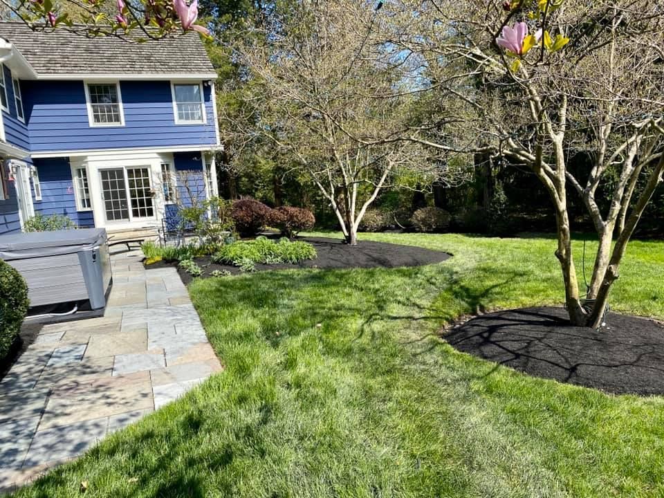 Blue house with stone walkway and green lawn, trees with dark mulch beds.