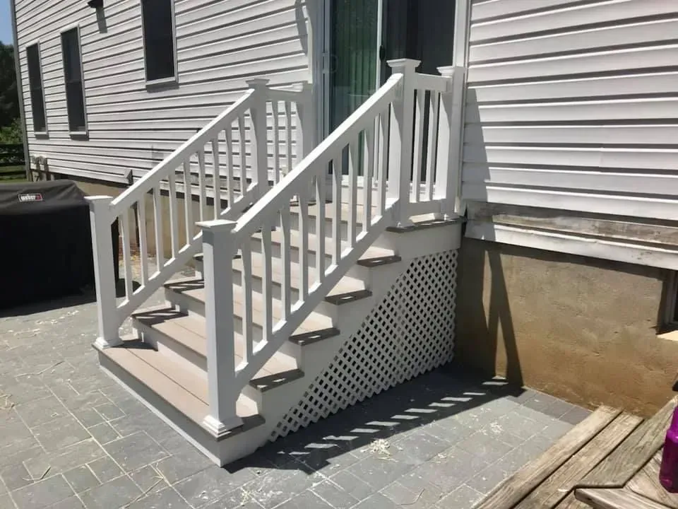 White stairs with a railing leading up to a house door, built on a patio.