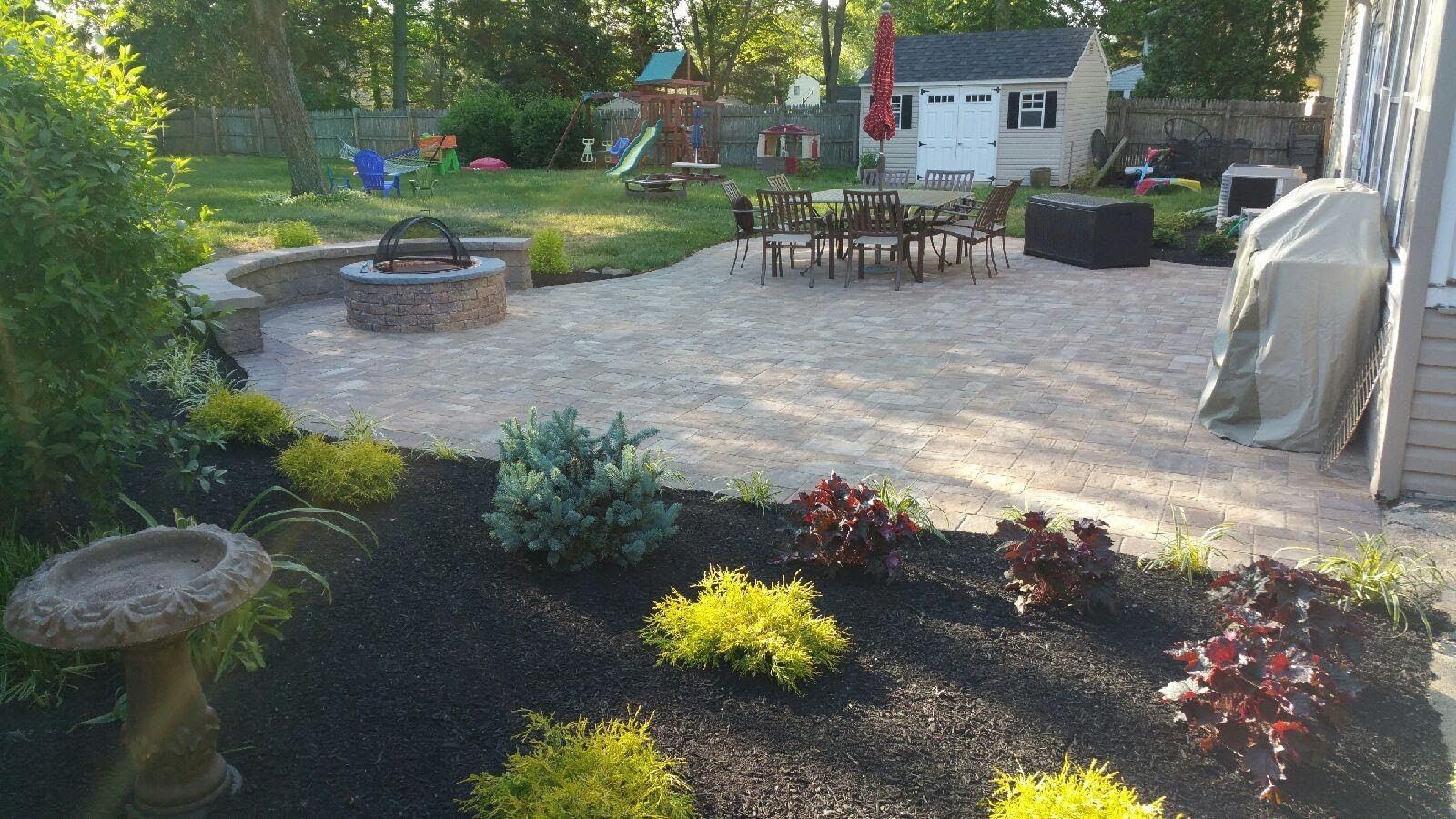Backyard patio with stone paving, fire pit, garden beds, and outdoor dining table under trees