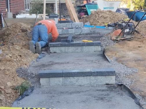 Worker smoothing concrete steps at a construction site with gravel and dirt around them