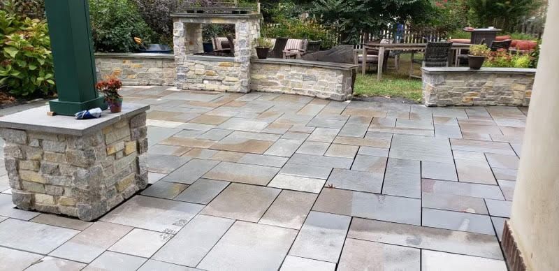 Stone patio with a built-in grill and seating area in a backyard garden