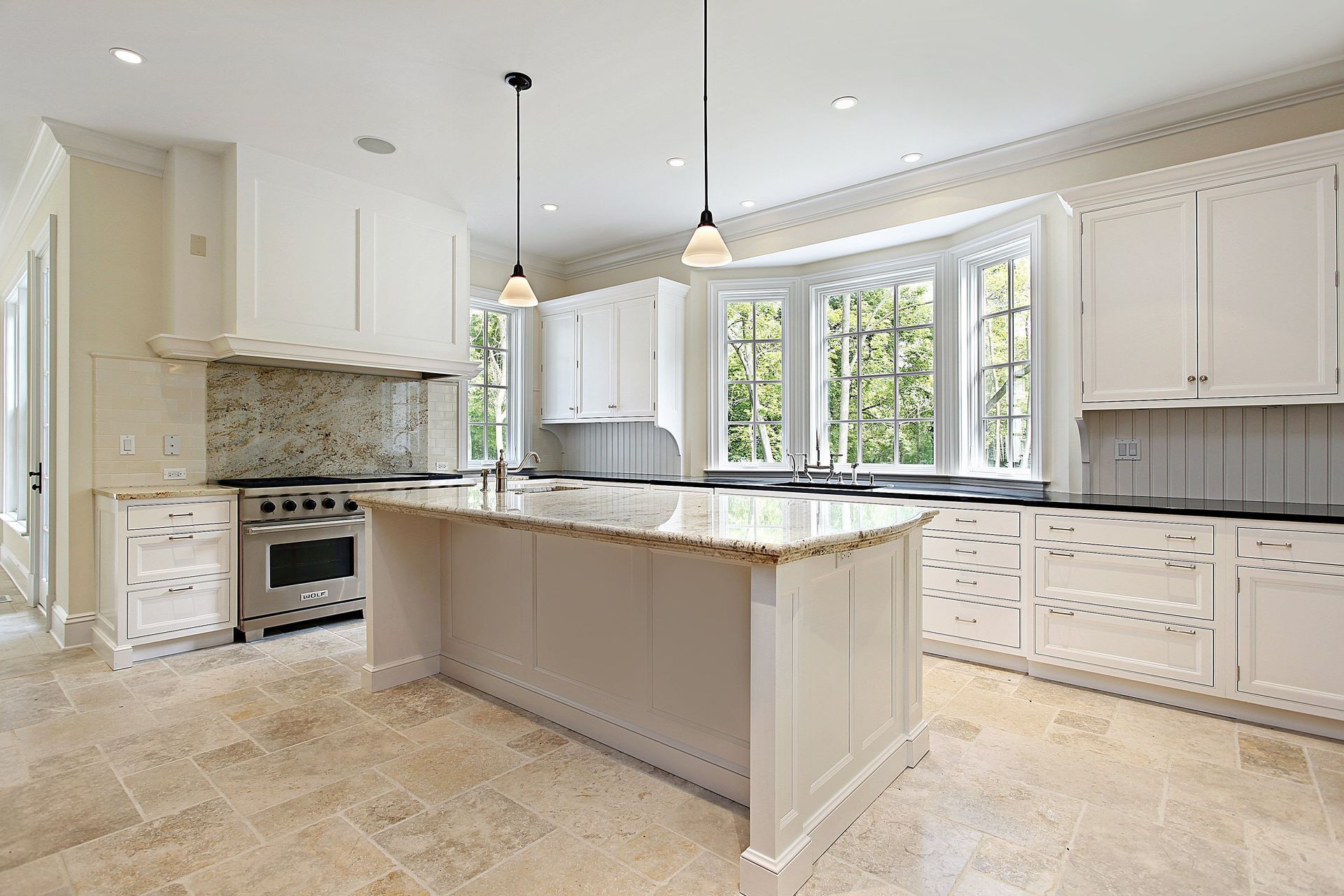 Bright white kitchen with marble island, tiled floor, and large windows overlooking greenery