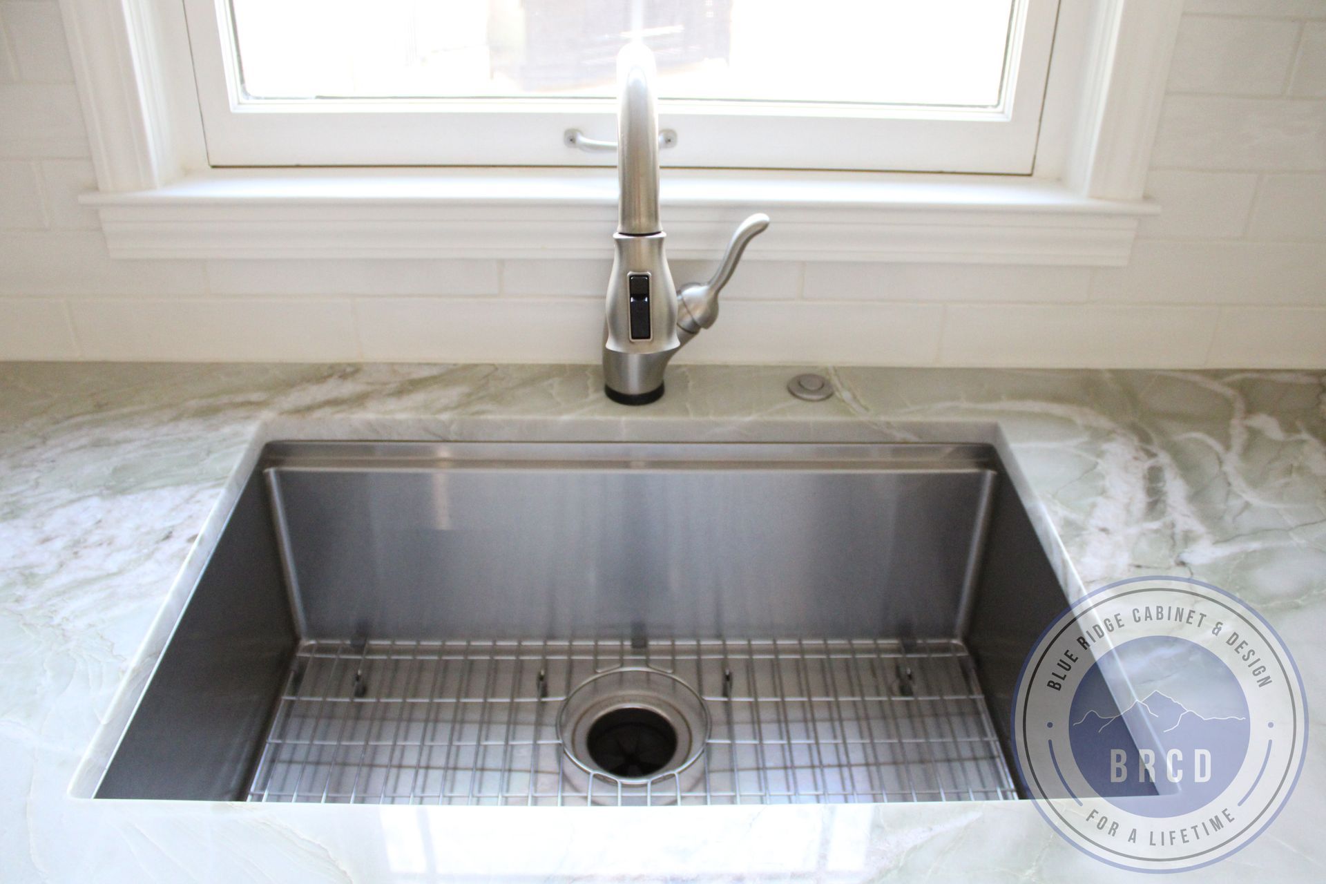 Stainless steel farmhouse sink under a window in a bright kitchen