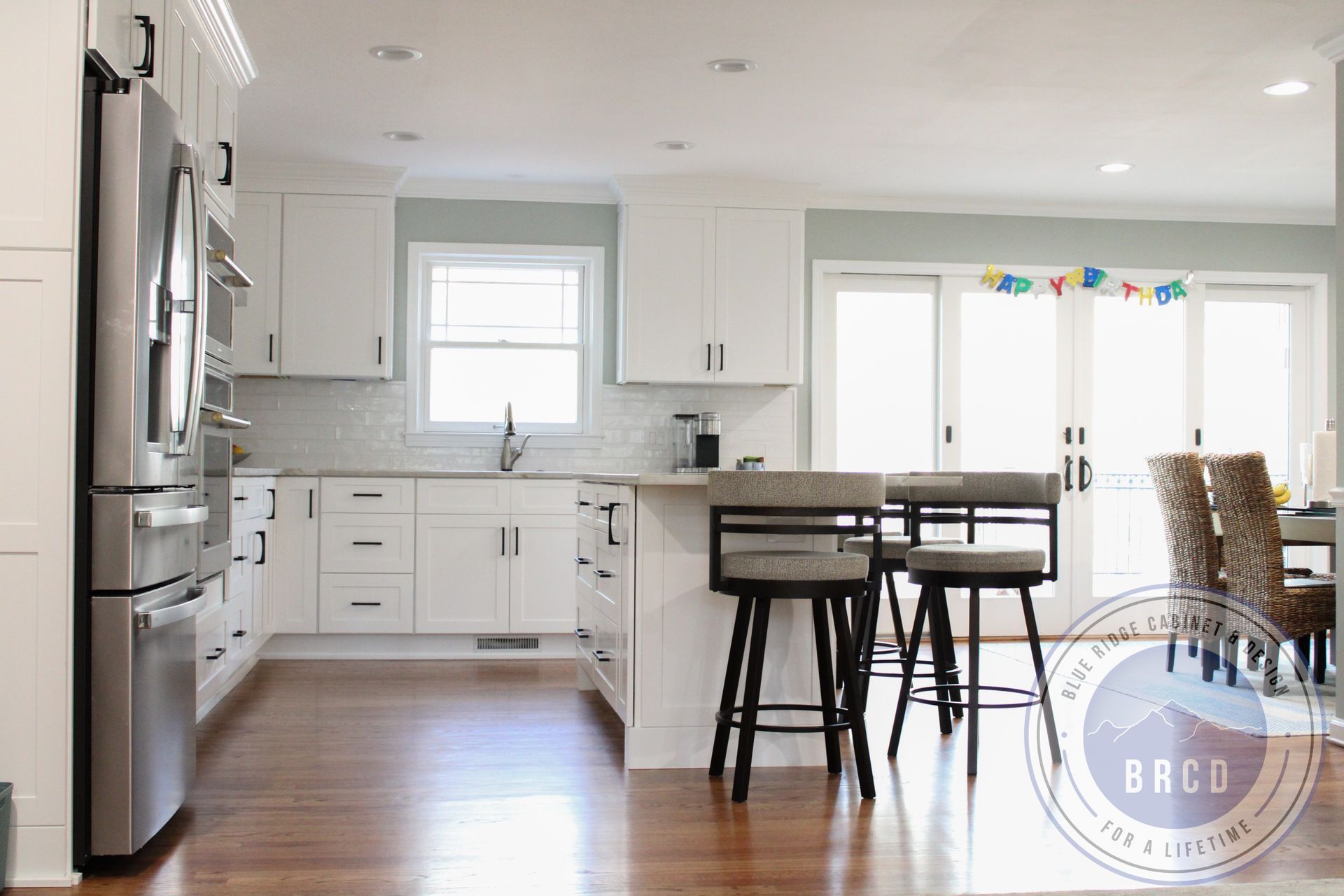 Bright modern kitchen with white cabinets, stainless appliances, island stools, and hardwood floors