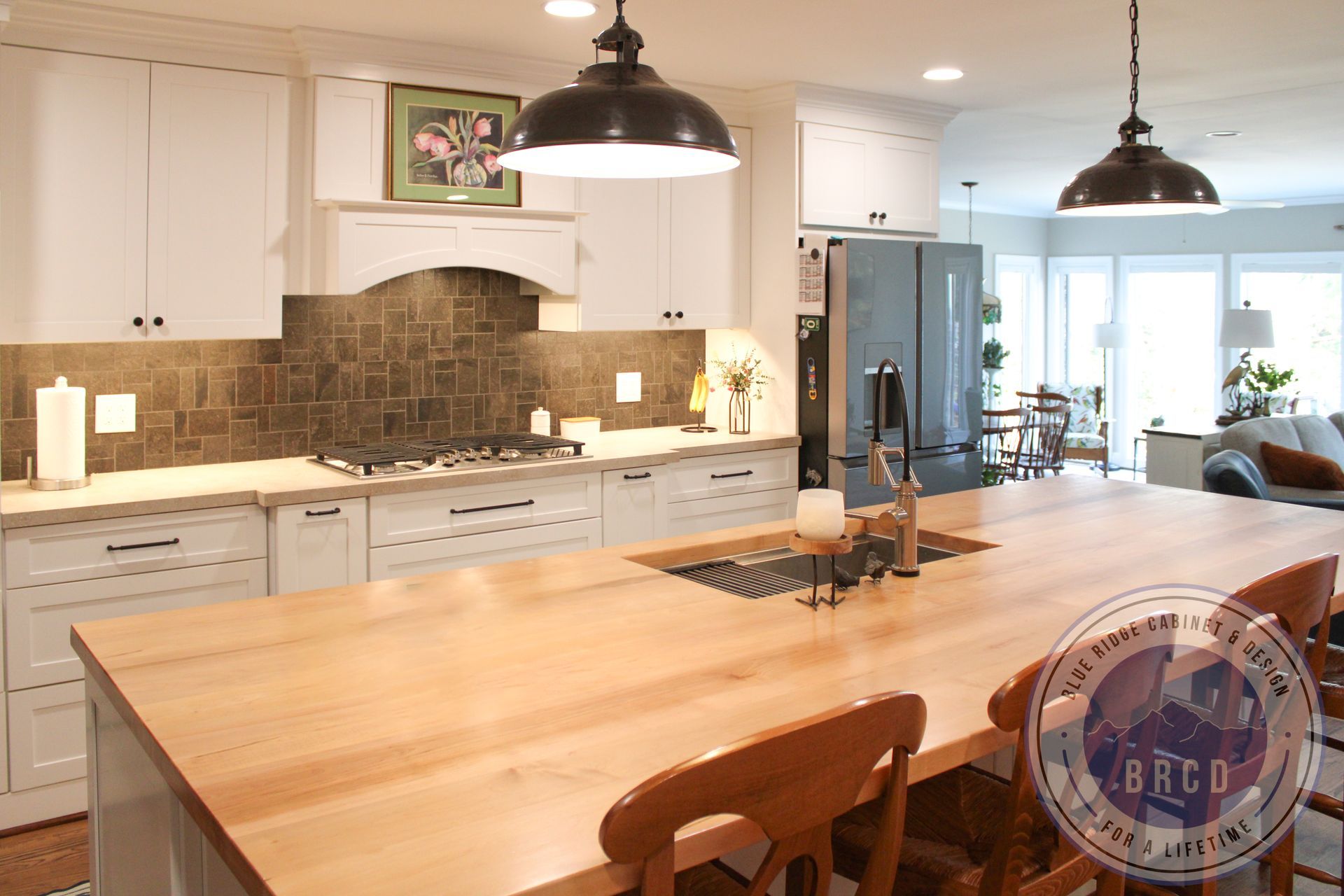 Bright modern kitchen with white cabinets, large wooden island, pendant lights, and dining area near windows