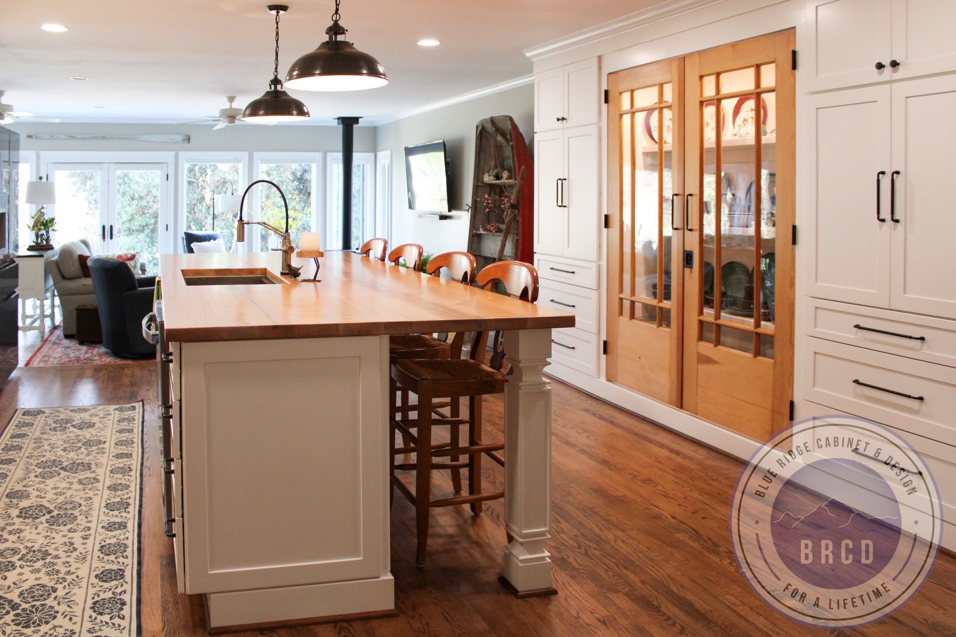 Bright kitchen with a large island, pendant lights, wood floors, and glass double doors to the right.
