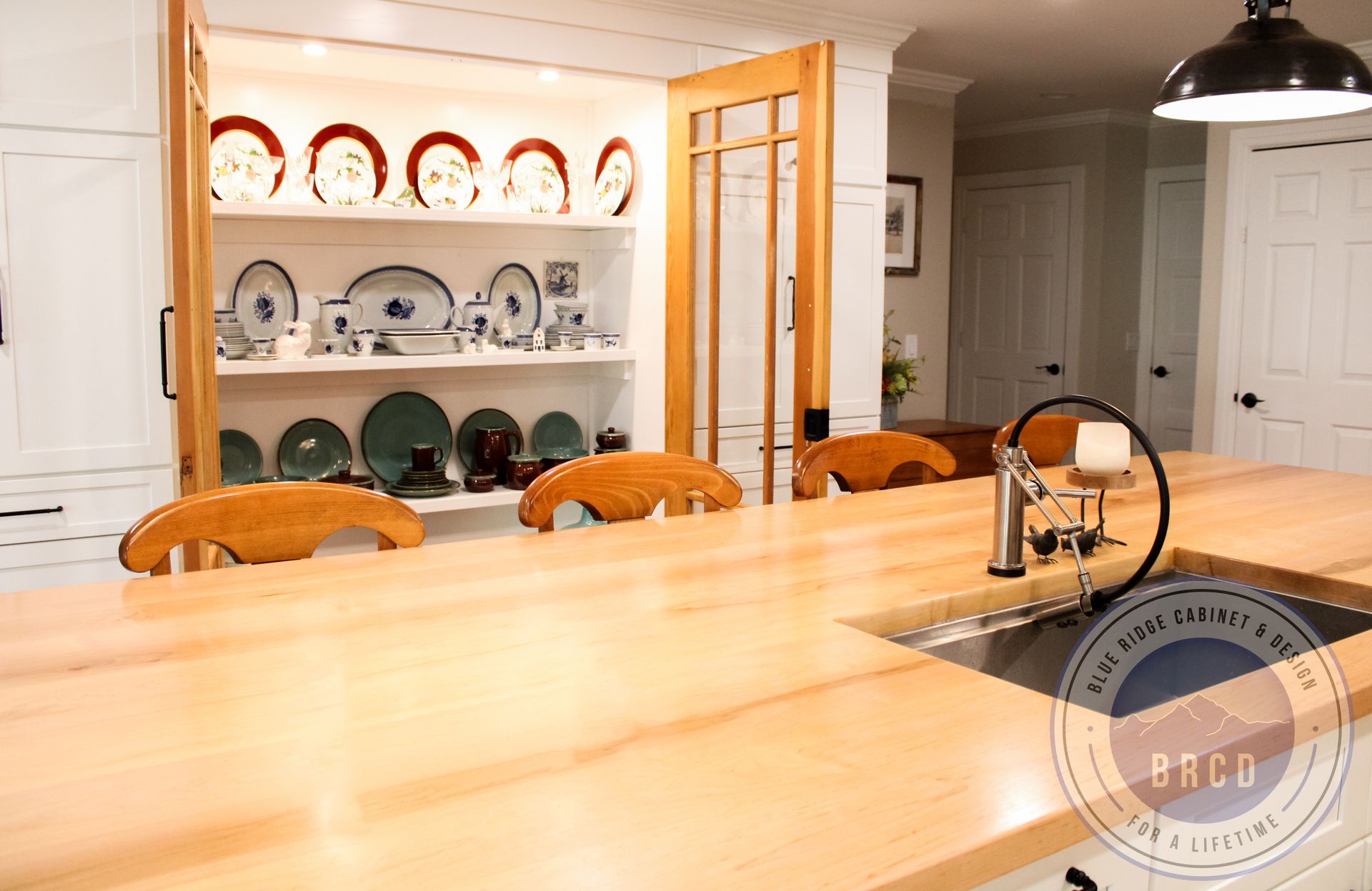 Bright kitchen with a large wooden island and shelves of decorative plates visible in the background