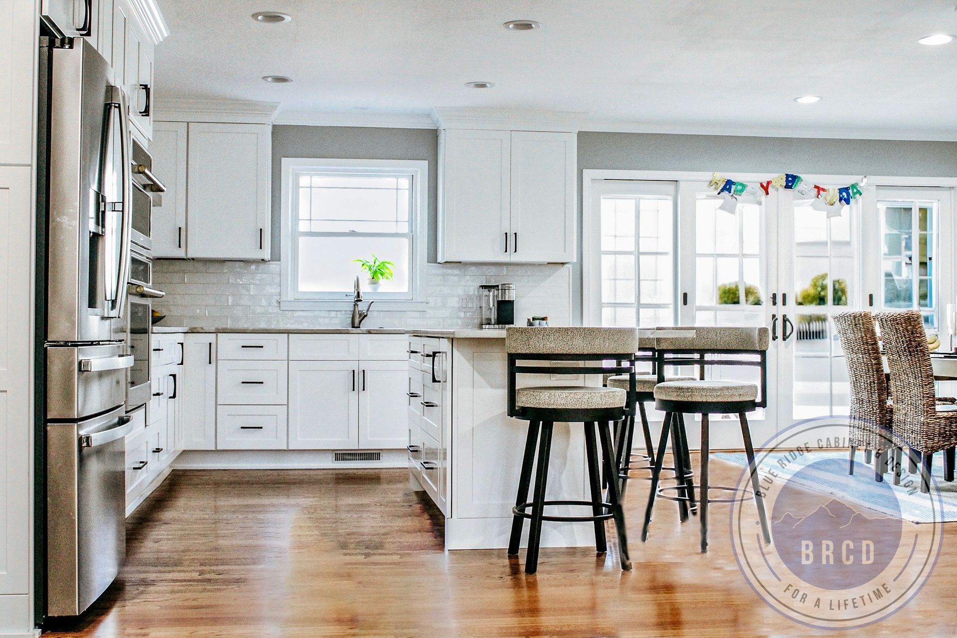 Bright white kitchen with island, stools, stainless fridge, and hardwood floors in a sunlit open layout