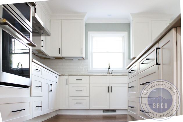 Bright white kitchen with cabinets, sink under window, stainless appliances, and wood floor