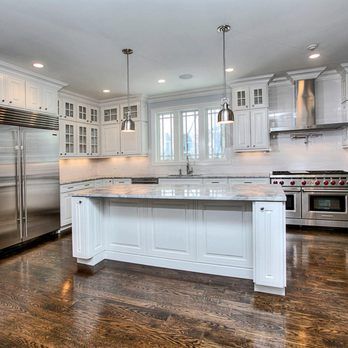 Bright white modern kitchen with large island, stainless steel appliances, and dark hardwood floors