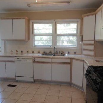 Empty white kitchen with tiled floor, window over sink, and black stove on the right