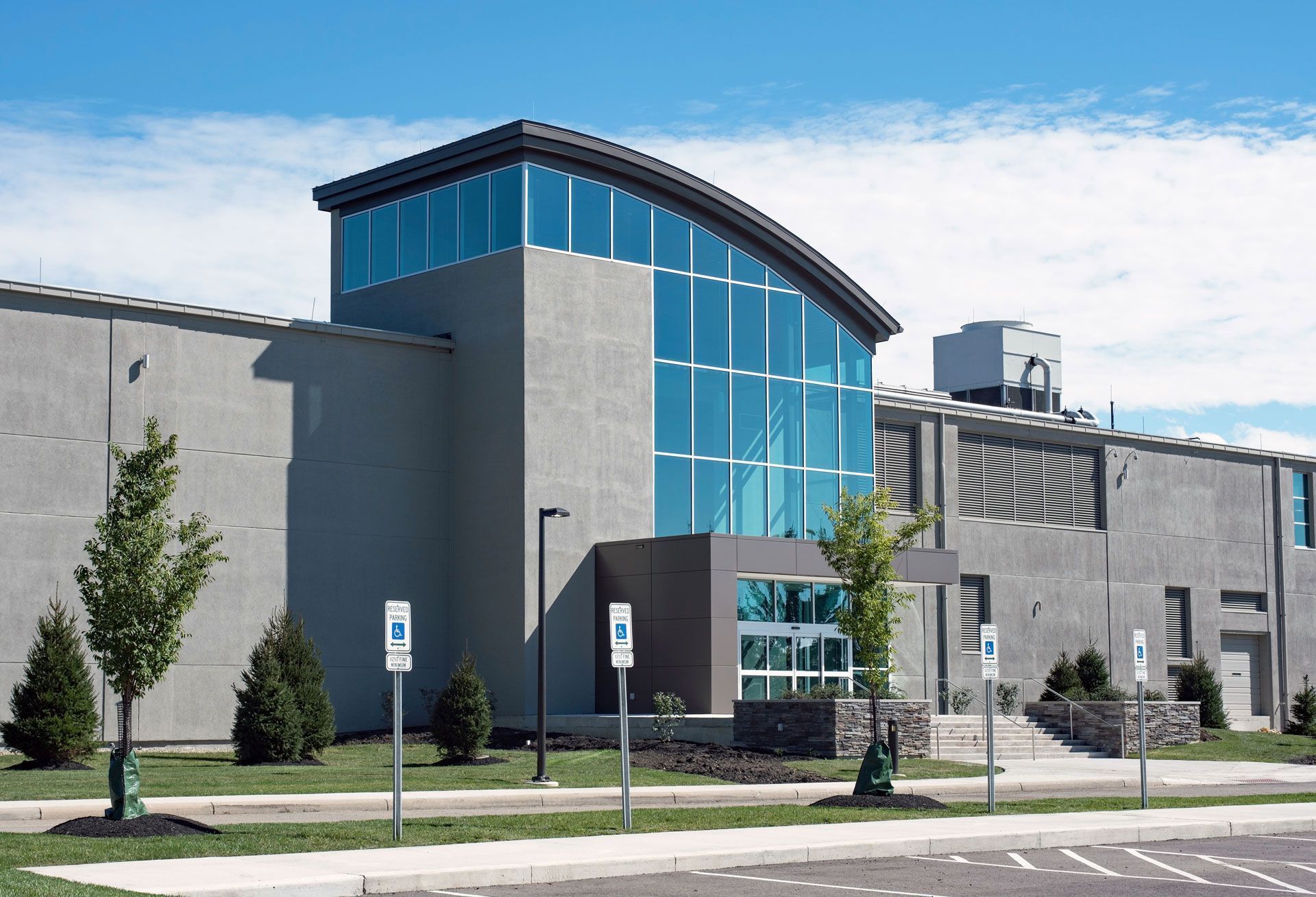 Modern gray building with a tall blue glass entrance and small landscaped lawn under a clear sky