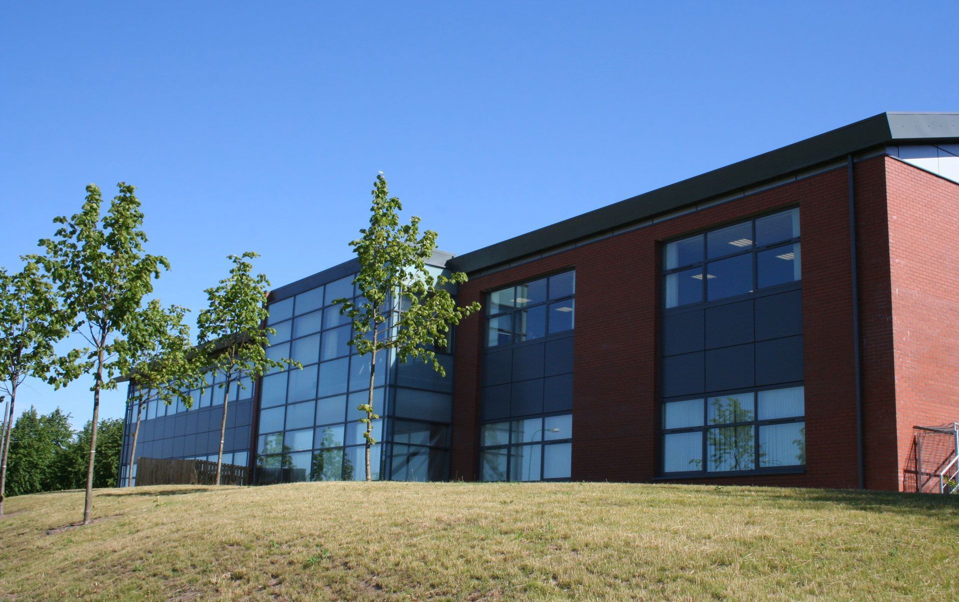 Modern brick-and-glass building on a grassy hill under a clear blue sky
