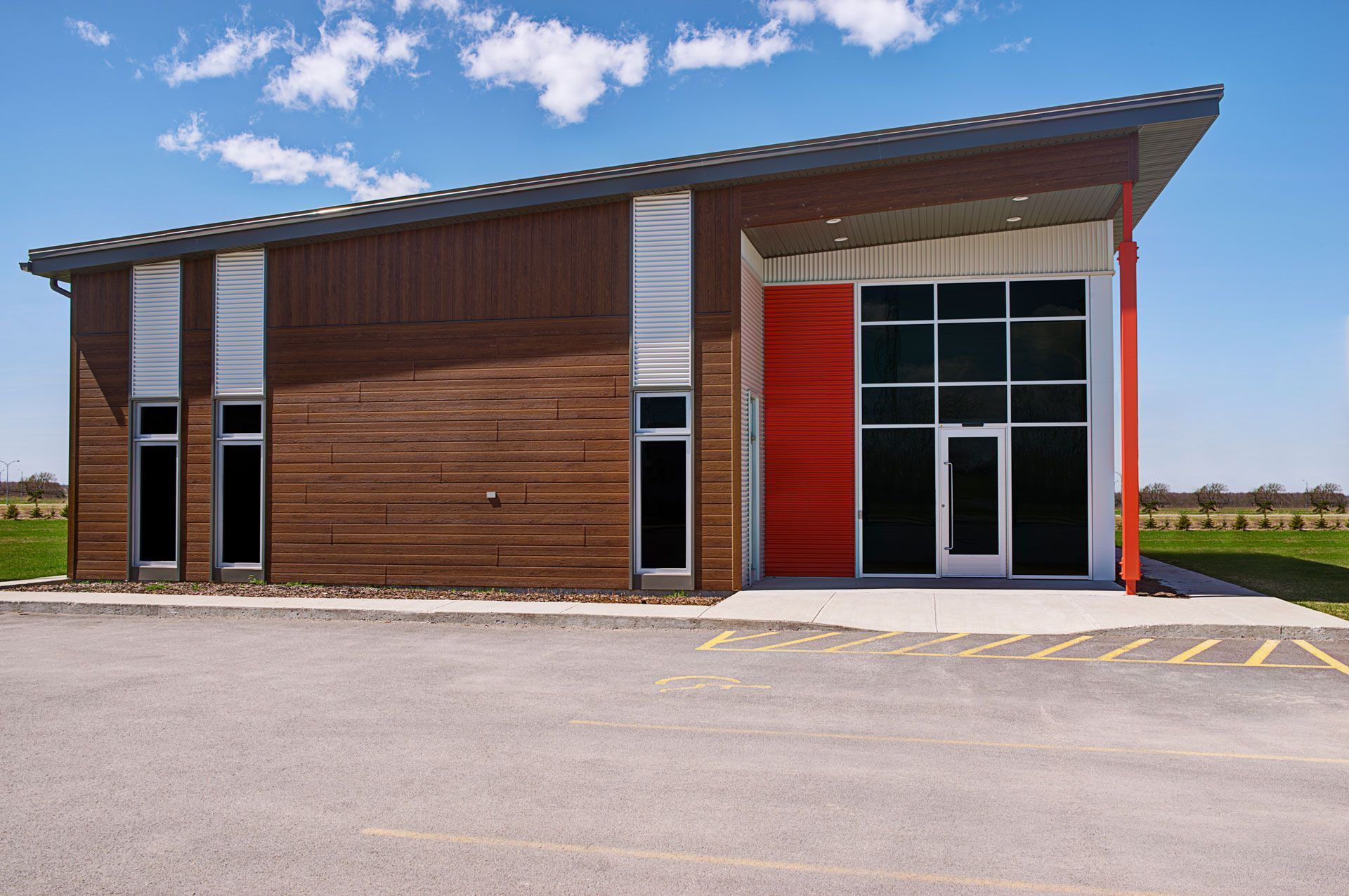 Small modern building with brown wood siding, red entrance, and large glass doors under a blue sky