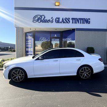 White sedan parked outside Blue's Glass Tinting storefront on a sunny day.