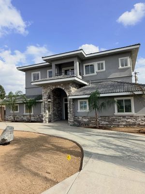 Large gray two-story house with stone entry and curved driveway under a blue sky