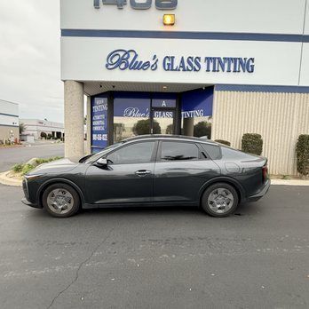 Dark gray sedan parked outside Blue’s Glass Tinting storefront.