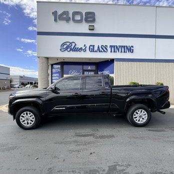 Black pickup truck parked outside Blues Glass Tinting storefront.