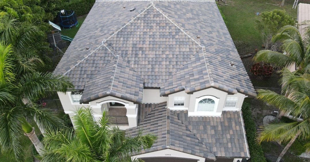 An aerial view of a large house with a roof surrounded by palm trees.